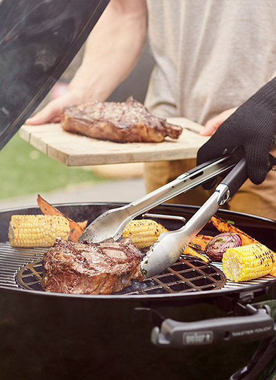 A picture of a BBQ being used to cook steak on a searing grate and vegetables